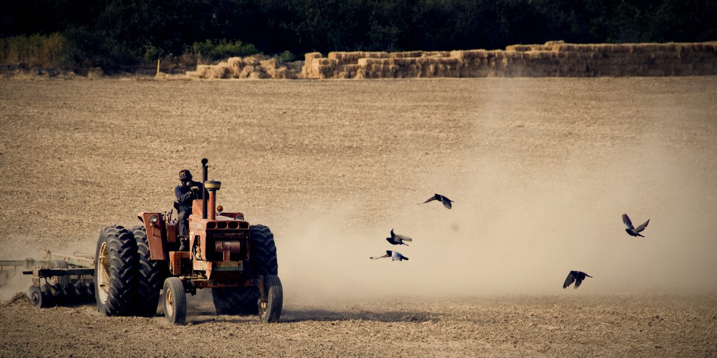 Traktor duke punuar tokën me pluhur në ajër